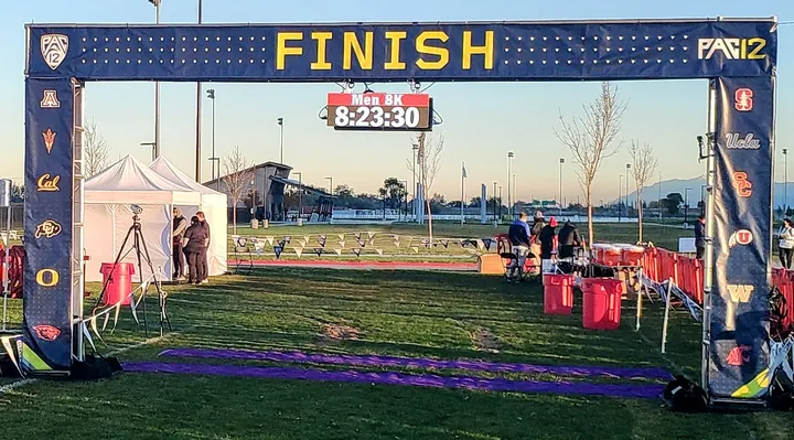 A race clock showing Men 8K and 8:23:30 hanging from a Pac-12 finish arch
