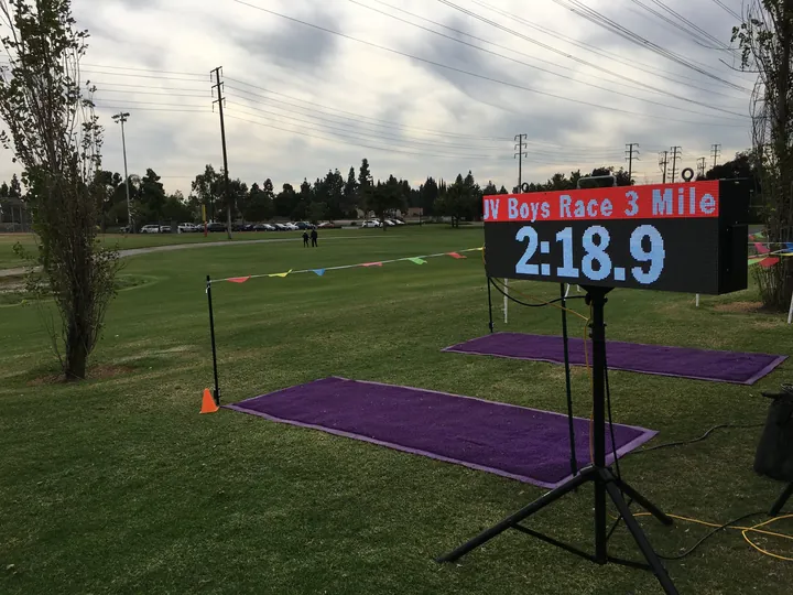 A race clock on its stand beside a cross country finish chute